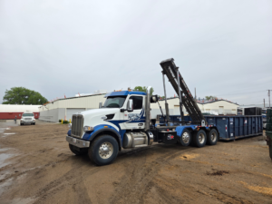A Miedema Sanitation Inc of Huron SD roll-off truck with a blue dumpster on a dirt lot in Mitchell, SD.