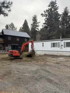 A mini-excavator clearing brush and debris near a residential property by HC Bar Excavation LLC in Bend, OR.