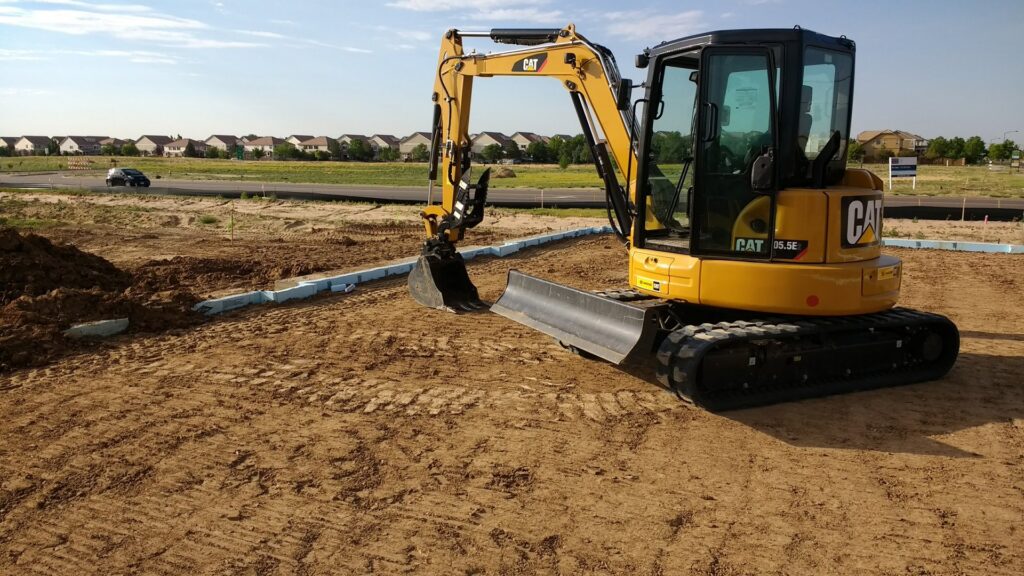 A yellow mini excavator on a construction site, performing site preparation for Aspen Excavation in Spokane, WA.