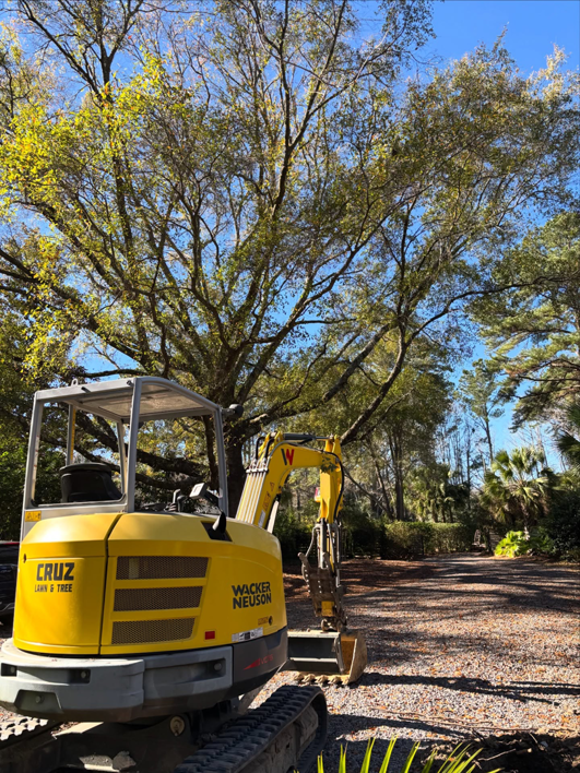 A yellow mini excavator, branded Cruz Lawn & Tree, used for tree removal in Charleston, SC.