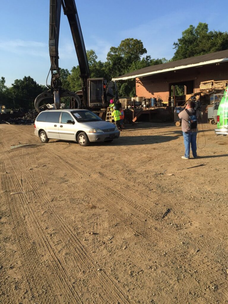 A silver minivan parked at the salvage yard with a large crane in the background at Queen City Metal Recycling & Salvage in Charlotte, NC.