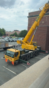 A large yellow mobile crane with outriggers extended, ready for heavy lifting at a job site by BURT crane & rigging in Green Island, NY.