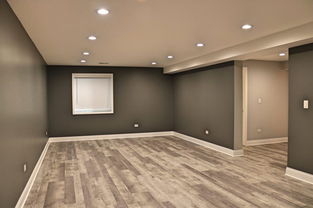 A modern basement living area with dark gray walls and new wood-look flooring by Grizzly Renovations in Naperville, IL