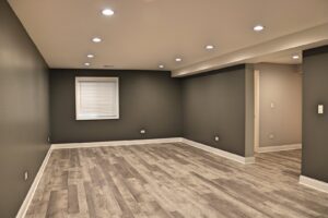 A modern basement living area with dark gray walls and new wood-look flooring by Grizzly Renovations in Naperville, IL