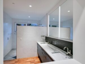 A luxurious modern bathroom with a double vanity, lighted mirrors, and a spacious walk-in shower by Transformations Custom Build in Austin, TX