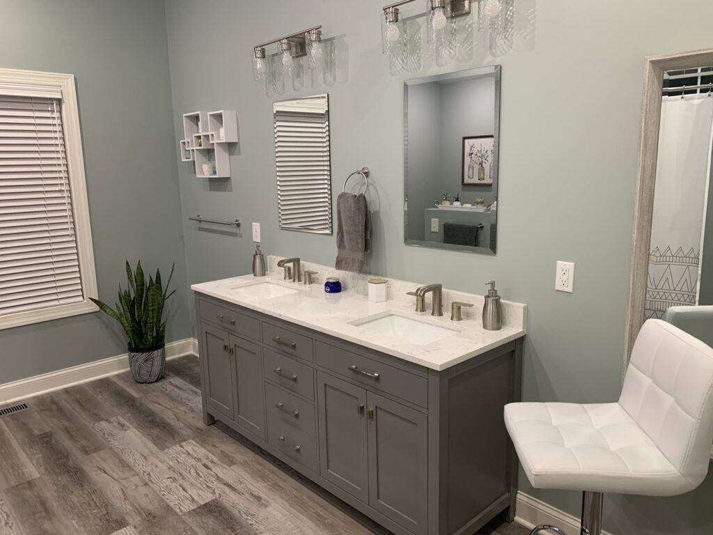 A modern bathroom featuring a double vanity, light green walls, and wood-look flooring, a project by Paradise Found Construction in Cary, NC.