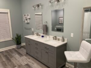 A modern bathroom featuring a double vanity, light green walls, and wood-look flooring, a project by Paradise Found Construction in Cary, NC.