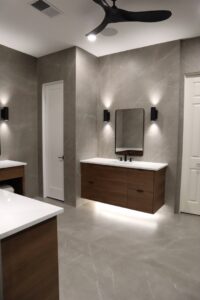 A modern bathroom remodel featuring a floating wood vanity, wall-mounted mirrors, and elegant grey marble-look tiles by Whole House Remodel & Design North Dallas Tx in Frisco, TX.