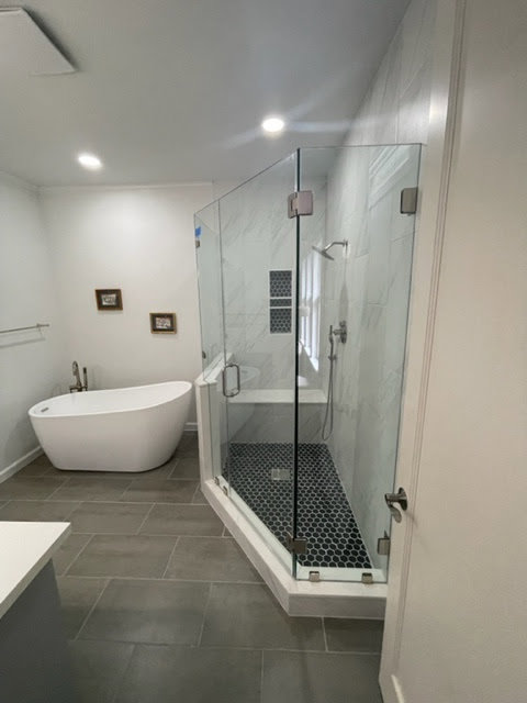 A modern bathroom remodel featuring a freestanding tub and a corner glass shower with hexagonal floor tiles by MC Master Construction in League City, TX