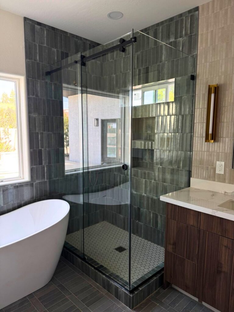 A modern bathroom remodel featuring a freestanding tub, glass shower, and dark tiled walls by LJ Builders in Chandler, AZ
