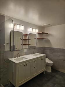 A modern bathroom remodel featuring a double vanity, new lighting, and floating shelves by Huynh Design & Remodeling in Alexandria, VA.