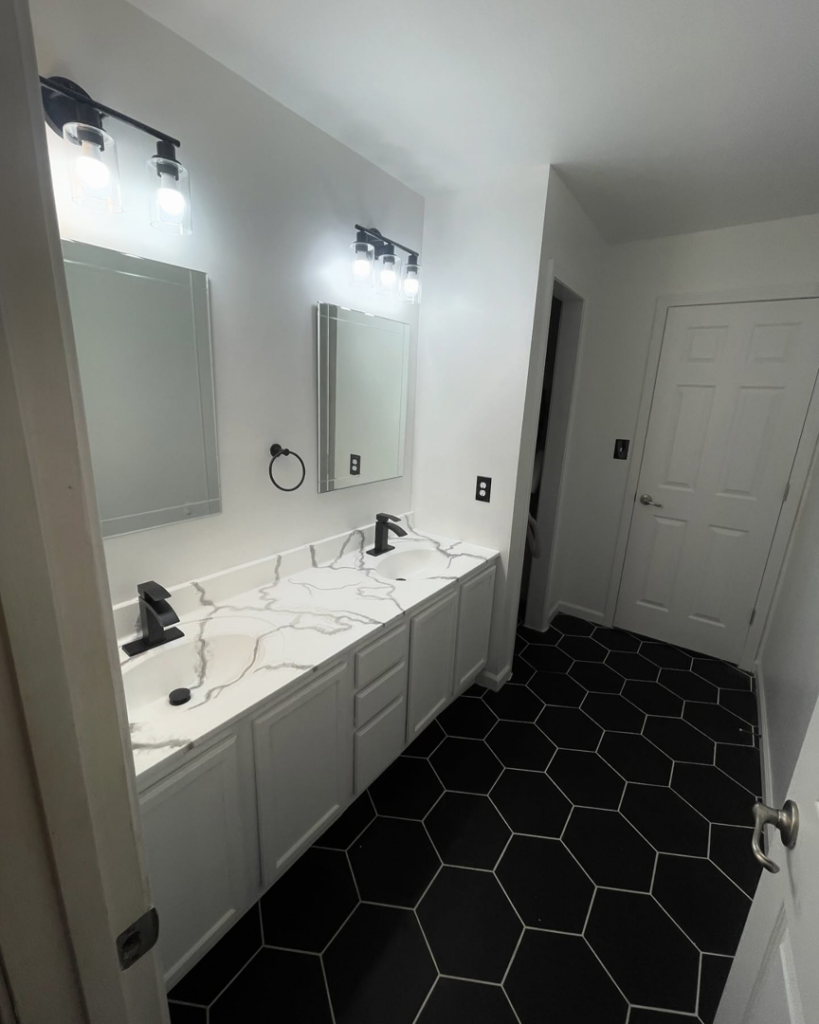 A modern bathroom remodel featuring a double vanity, black fixtures, and hexagonal floor tiles by Make It Happen Homes STL in St. Louis, MO.