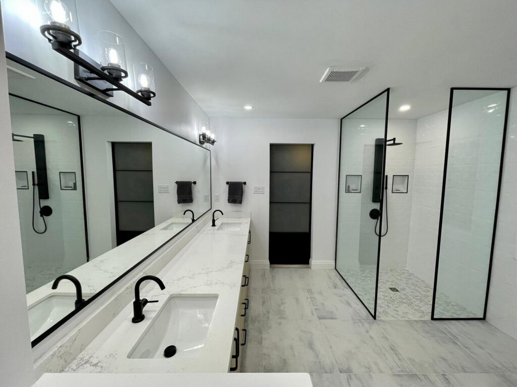 A modern bathroom remodel with a double vanity, large mirror, and walk-in glass shower by NP General Contracting in Austin, TX.