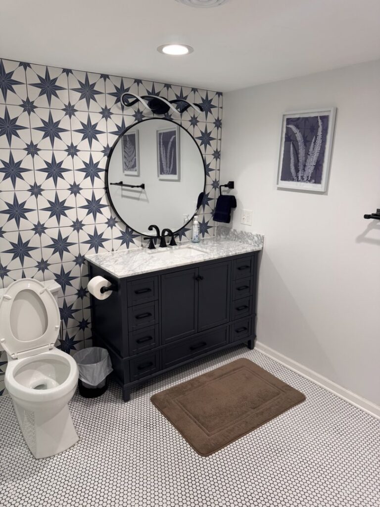 A beautifully remodeled modern bathroom featuring a dark vanity, round mirror, and patterned wall tiles by Inova Builds in Bloomington, MN.