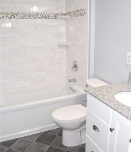 A newly remodeled modern bathroom with a white tub, toilet, and granite vanity by Ready & Able in Etters, PA.