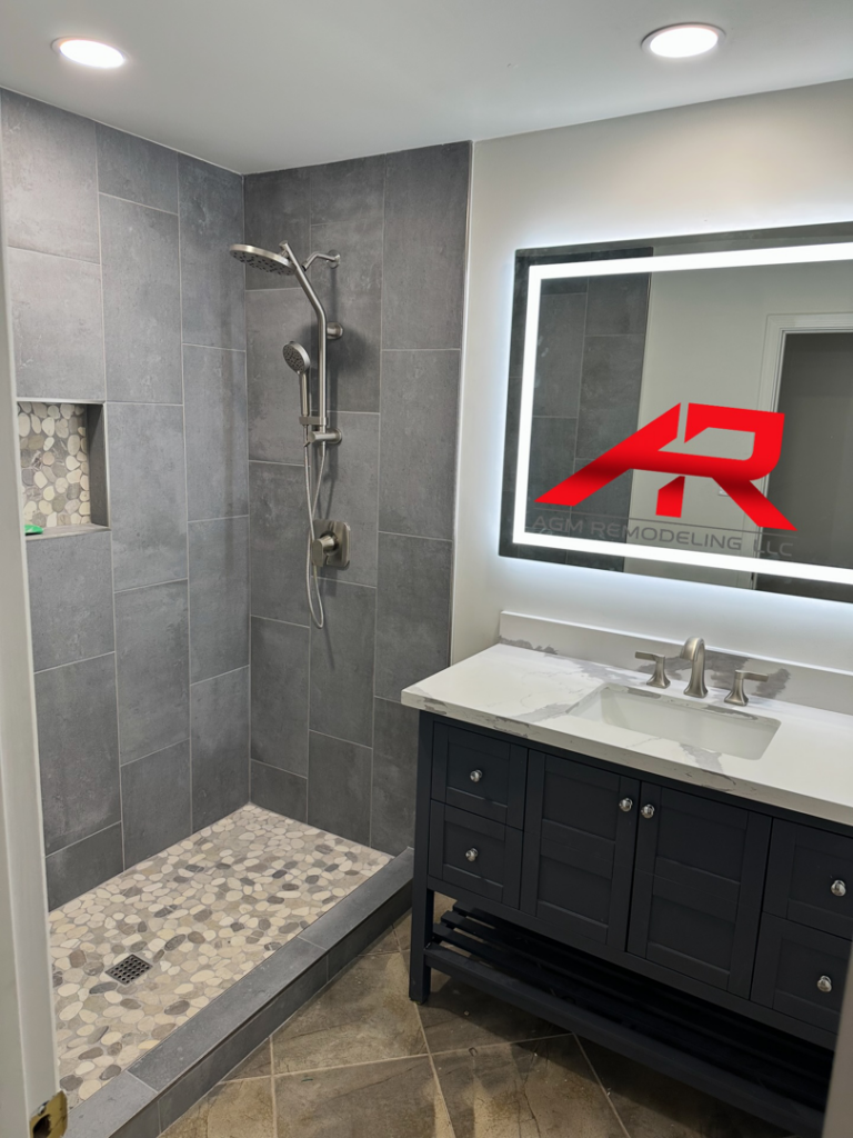 A modern bathroom remodel showcasing a walk-in shower with grey tiles and a new vanity with an illuminated mirror by AGM Remodeling LLC in Scottsdale, AZ.