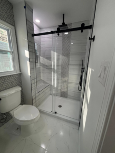 A modern bathroom remodel featuring a new walk-in shower with glass doors and a toilet by JJConstruction203 LLC in Charlotte, NC.