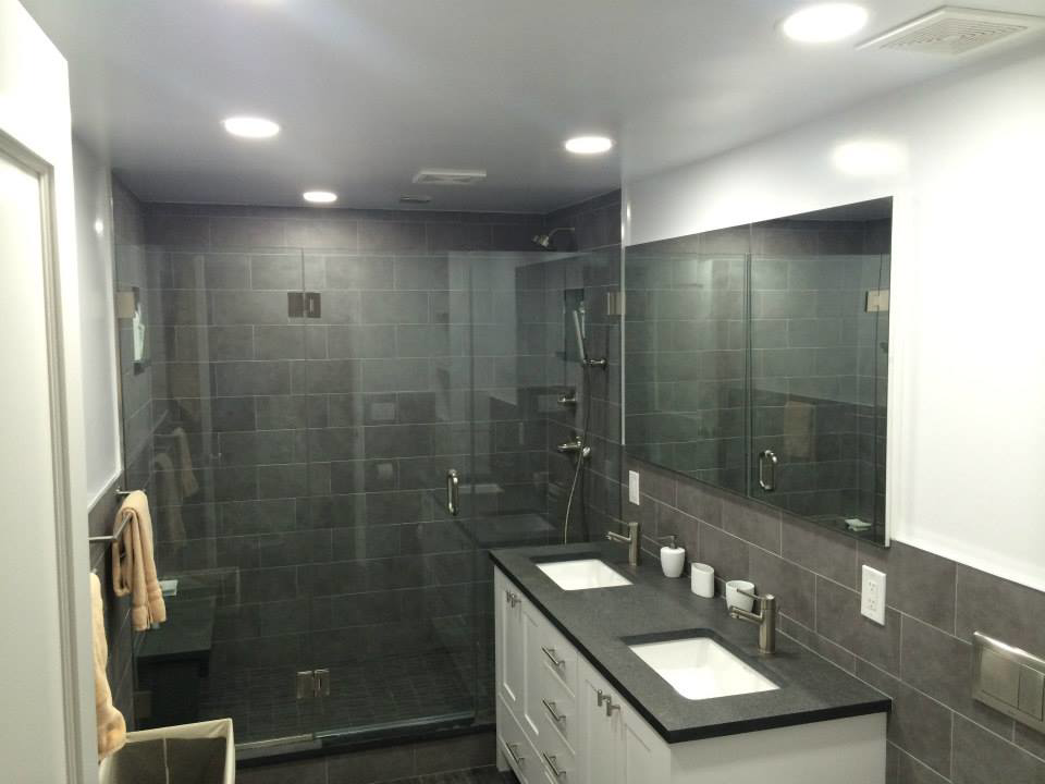 A fully renovated modern bathroom featuring a double vanity, tiled shower, and recessed lighting by Executech Interiors in Yonkers, NY