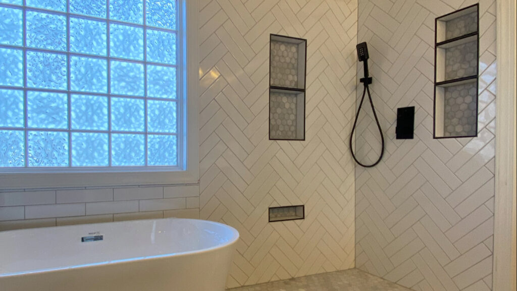 A modern bathroom renovation featuring a freestanding tub and herringbone pattern wall tiles by Goubar Tile And More in Raleigh, NC.