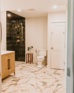 A beautifully completed modern bathroom renovation featuring a dark tiled shower and marble-look floor by Knaub Home Solutions in Rochester, NY.