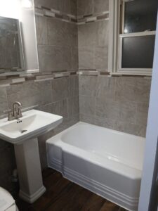 Modern bathroom renovation with new tub, pedestal sink, and grey tiled walls by Phillys Finest Tub & Tile Refinishing in Philadelphia, PA