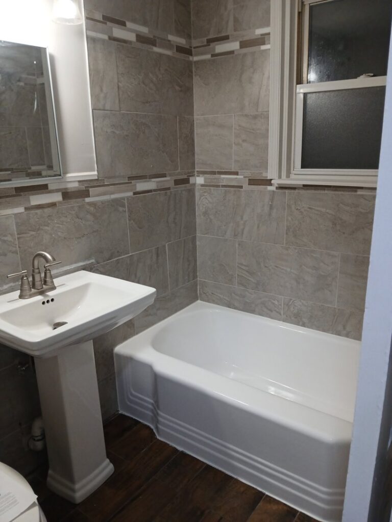 Modern bathroom renovation with new tub, pedestal sink, and grey tiled walls by Phillys Finest Tub & Tile Refinishing in Philadelphia, PA