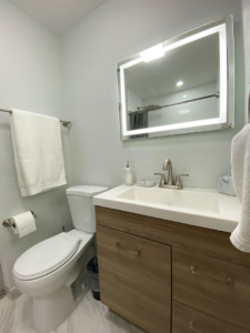 A modern bathroom renovation featuring a wood vanity and lighted mirror by Property Solutions Network, Llc in Hialeah, FL