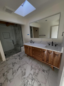 A modern bathroom renovation showcasing a double vanity, large mirror, and glass shower by Raven Construction LLC in Tucson, AZ.
