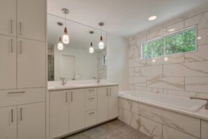 A modern bathroom renovation featuring a double vanity and tiled bathtub by Stone Age Granite of Austin, TX.