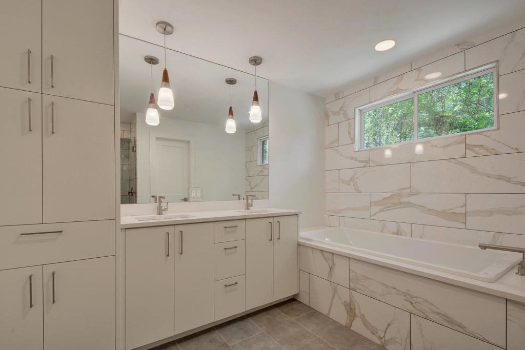 A modern bathroom renovation featuring a double vanity and tiled bathtub by Stone Age Granite of Austin, TX.