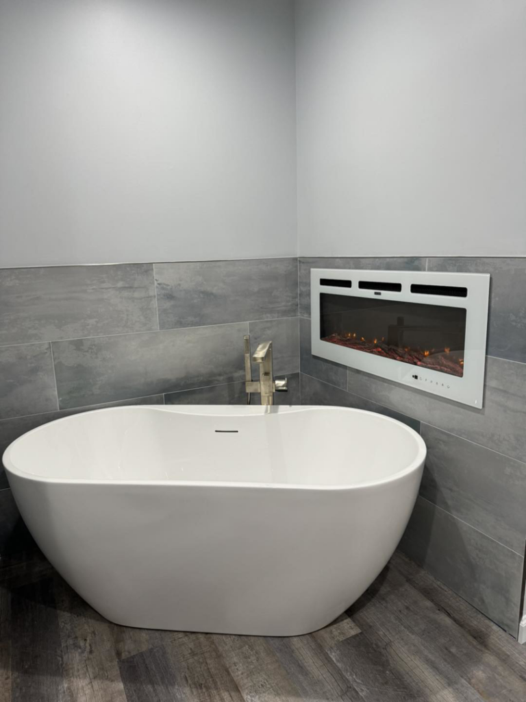 A modern bathroom renovation featuring a freestanding tub, tiled walls, and an electric fireplace by Strausbaugh Construction Services LLC in Cincinnati, OH.