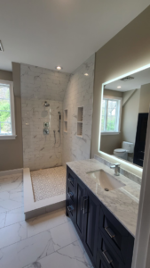A modern bathroom renovation showcasing a walk-in tiled shower, new vanity, and illuminated mirror by David Hayden Construction LLC in Danbury, CT.