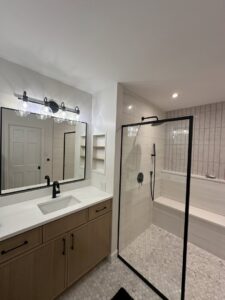 A modern bathroom renovation featuring a wood vanity, large mirror, and a walk-in shower with white tile by Westrick Homes in St. Louis, MO.
