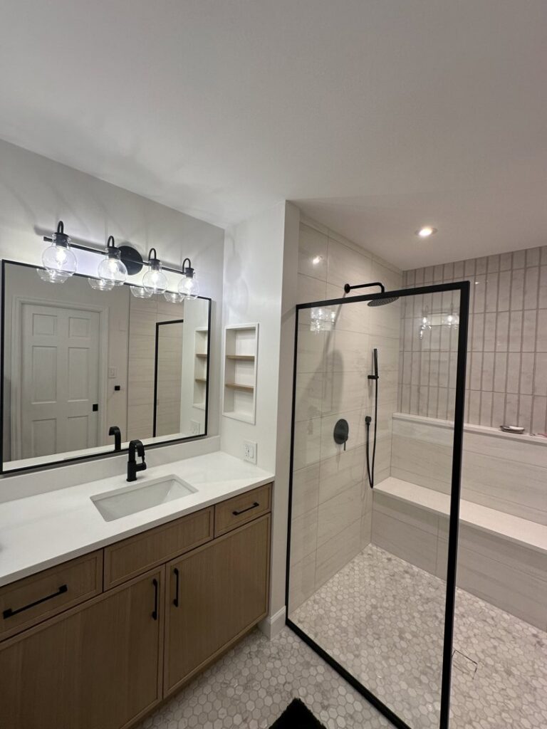 A modern bathroom renovation featuring a wood vanity, large mirror, and a walk-in shower with white tile by Westrick Homes in St. Louis, MO.