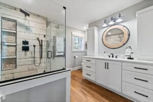 A modern bathroom renovation featuring a glass-enclosed shower and a white vanity with a round mirror, completed by Orion Construction Services in Duluth, MN.