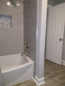 A modern bathroom renovation featuring gray tiled walls, new bathtub, and wood-look tile flooring by Brothers Home Improvement in East Hartford, CT
