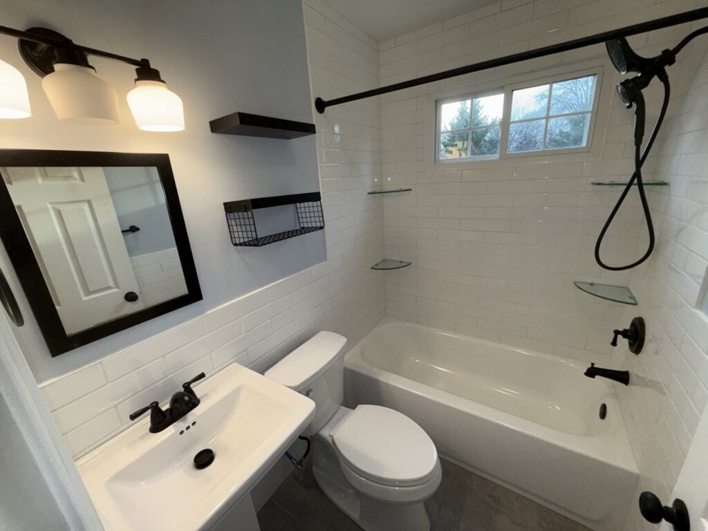 A modern bathroom renovation showcasing white subway tiles, a pedestal sink, and black fixtures completed by MPH Design in Philadelphia, PA.