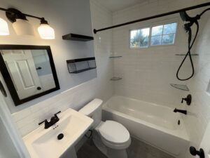 A modern bathroom renovation showcasing white subway tiles, a pedestal sink, and black fixtures completed by MPH Design in Philadelphia, PA.