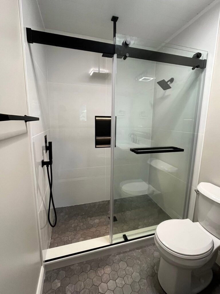A modern bathroom with a black-framed sliding shower door and hexagonal floor tiles by Four Seasons Building & Remodeling in Mauldin, SC.