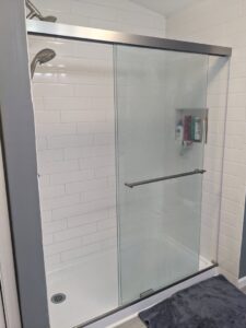 A modern bathroom shower featuring white subway tiles and a sleek glass door, renovated by Pink Rose Home Service in Rochester, NY.