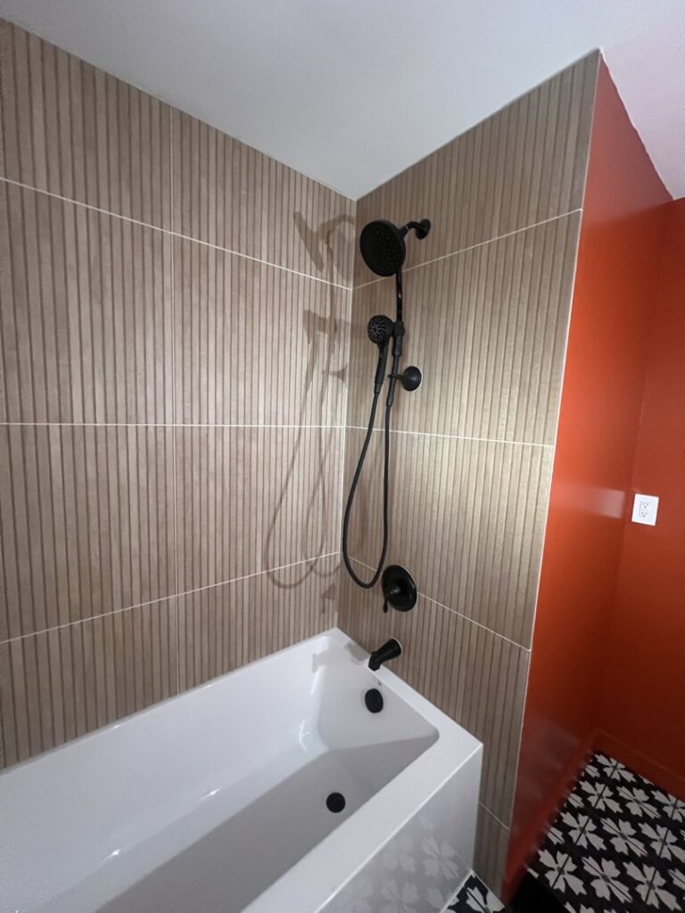 A modern bathroom shower and tub area featuring new vertical tile and black fixtures, remodeled by Gold-Mine Construction, LLC in Pittsburgh, PA.