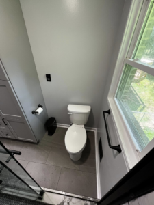 A newly renovated modern bathroom toilet area with grey walls and dark floor tiles by Simko Tile & Bath in Macon, GA.