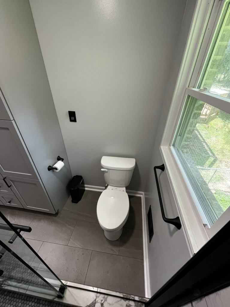 A newly renovated modern bathroom toilet area with grey walls and dark floor tiles by Simko Tile & Bath in Macon, GA.