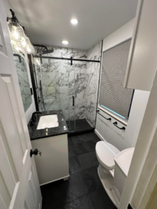 A modern bathroom featuring a toilet, vanity, and glass shower enclosure by Tap & Tile Inc. in East Pittsburgh, PA.