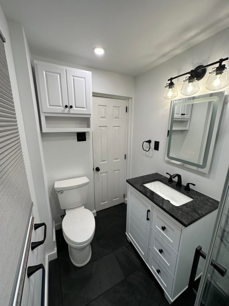 A modern bathroom featuring a toilet, vanity, and sleek black floor tiles by Tap & Tile Inc. in East Pittsburgh, PA.