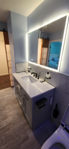 A modern bathroom vanity with a new sink, black fixtures, and illuminated mirror installed by Done Right Construction in Johnston, IA.