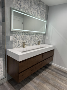 A modern bathroom vanity with a double sink, illuminated mirror, and tiled backsplash installed by Strausbaugh Construction Services LLC in Cincinnati, OH.
