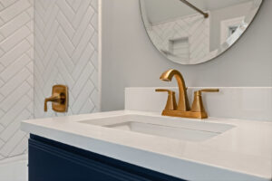 A modern bathroom vanity with a dark blue cabinet and gold faucet, part of a renovation by Integrated Contracting and Renovations in Pittsburgh, PA.