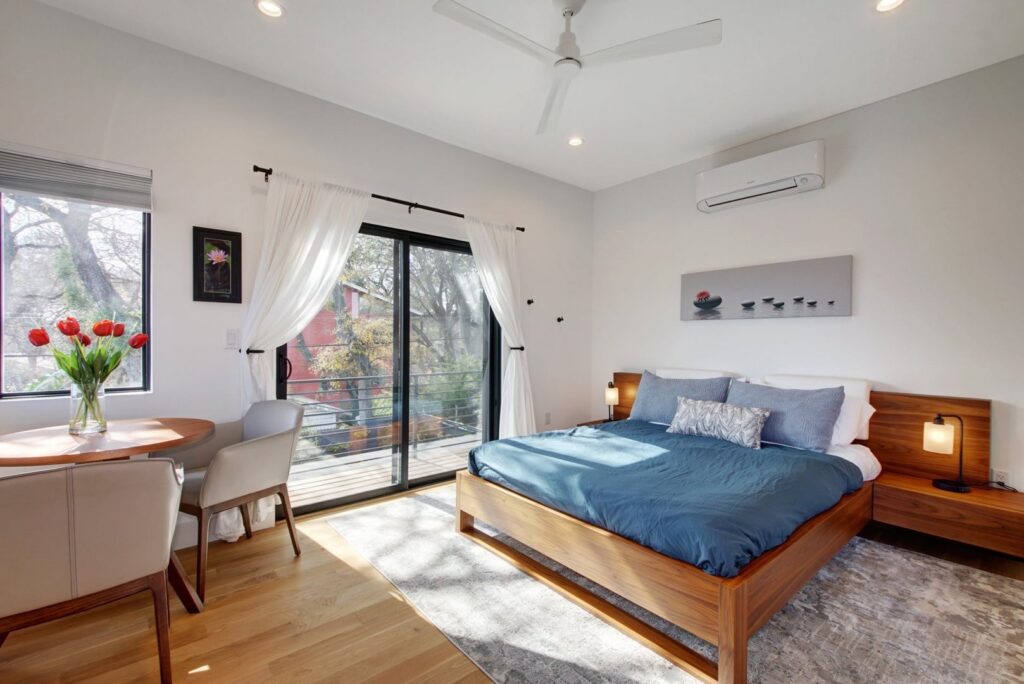 A modern bedroom with a wooden bed frame and sliding glass doors leading to a private balcony by Transformations Custom Build in Austin, TX