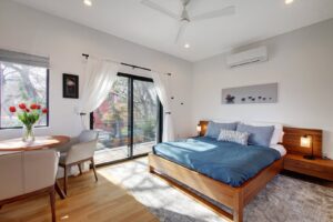 A modern bedroom with a wooden bed frame and sliding glass doors leading to a private balcony by Transformations Custom Build in Austin, TX